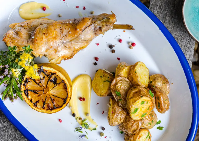 Confierte Kaninchenkeule, gegrillte Zitrone, Ofenkartoffeln und geräucherte Knoblauch-Mayo auf einem Teller