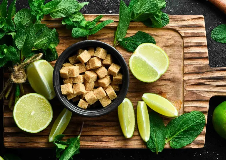 Zutaten für einen Cocktail mit geviertelten Limetten, braunem Zucker und frischer Minze angeritet auf einem Holzbrett