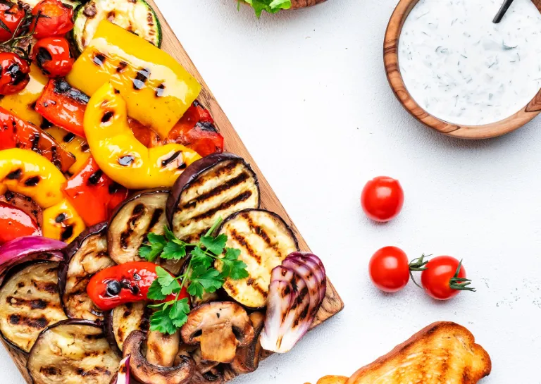 Grillgemüse Salat angerichtet auf einer hellen Tischplatte mit Kräuterquark, Tomaten und Brot 