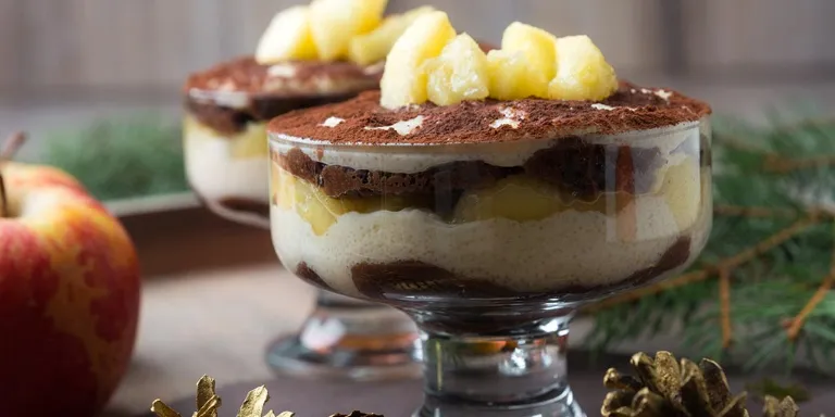 Tiramisu mit Bratapfel in einem hohen Dessertschälchen geschichtet mit Kakao und Apfelstückchen garniert. 