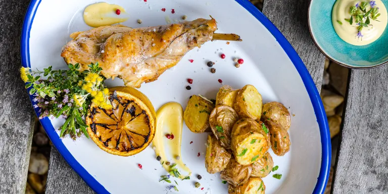 Confierte Kaninchenkeule, gegrillte Zitrone, Ofenkartoffeln und geräucherte Knoblauch-Mayo auf einem Teller