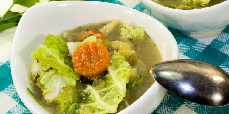 Wirsingsuppe mit Parmesan und Möhren angerichtet in einer kleinen Schale auf einer blau-weiß karierten Tischdecke