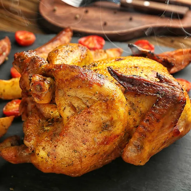 ganzes gegrilltes Hähnchen auf einem Schieferuntergrund mit Tomaten